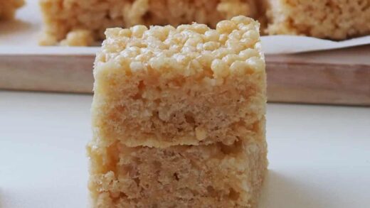 Two pieces of Rice Bubble Slice on top of each other. In the background is a timber tray with more pieces.