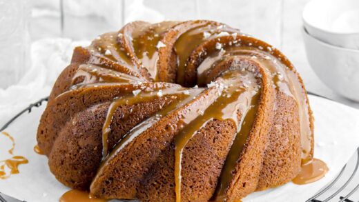 caramel sauce and flaked salt on top of bundt cake on wire cooling rack with empty glasses behind.