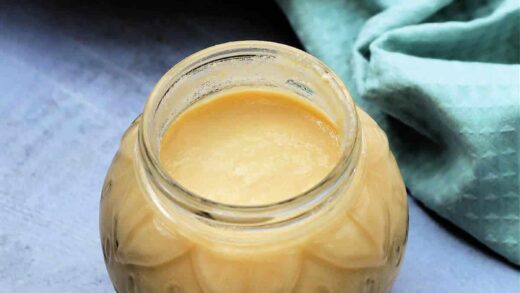 Open jar of pear curd with green cloth and pears in background.