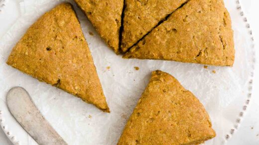 overhead view of triangular healthy pumpkin scones with spices and oats on a white plate along with a butter knife – quick and easy recipe – low fat, low calorie, egg free, and clean eating with vegan, gluten free, whole wheat, and dairy free options – made with no heavy cream or refined sugar