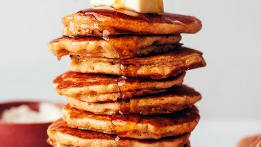 Pouring maple syrup onto a stack of fluffy gluten-free pancakes