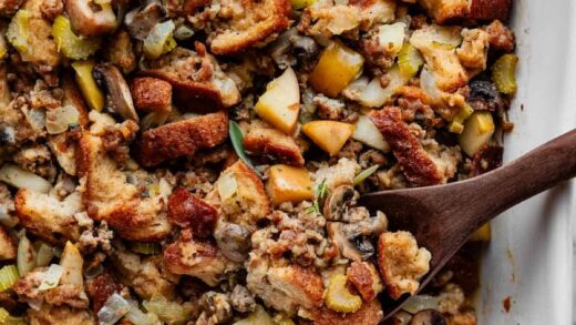 sausage herb Thanksgiving stuffing in a white baking dish with wooden spoon.