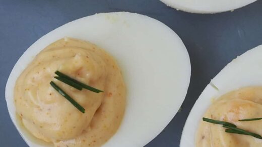 Close up of Curried Eggs topped with chives on a blue plate.