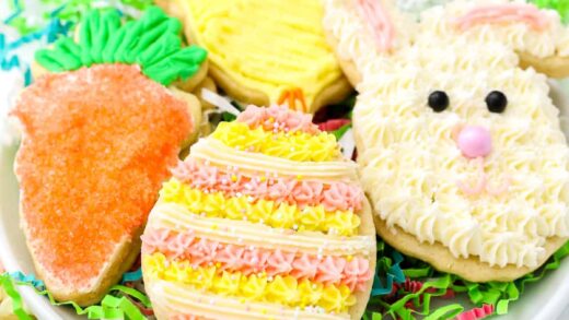 Frosted Easter sugar cookies shaped like a bunny, egg, chick, and carrot on a plate, nestled in green paper grass.