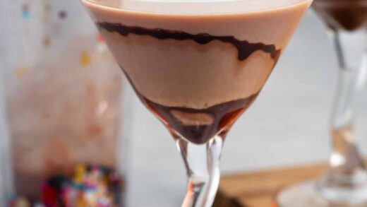 peanut butter martini in a clear tall glass with a peanut butter cup on the rim.