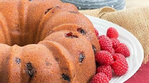 Raspberry Amaretto Bundt Cake on a cake plate with fresh raspberries.