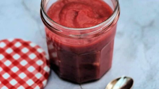 Jar of cranberry curd with lid to left and spoon in front.