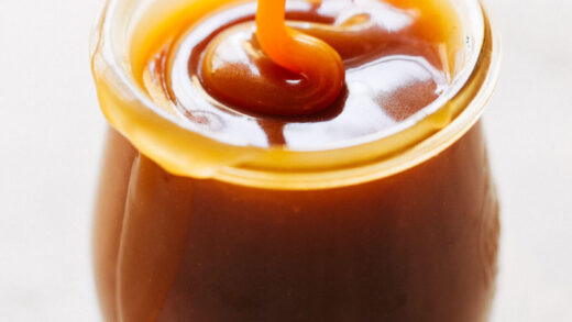 a jar of homemade salted caramel with a spoon drizzling caramel into it