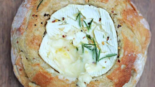 Melting baked camembert cheese in a bread bowl on wooden board.