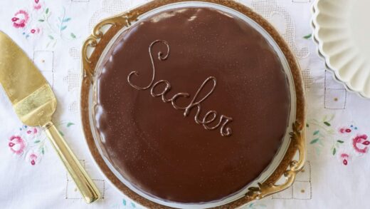 Classic Austrian Sacher Torte is placed on a round golden rim platter. It shows the silky smooth, shinny glaze.