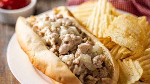 Homemade chicken cheesesteak on a white plate with potato chips and ketchup.