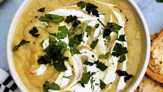 Bowl of potato leek soup garnished with swirls of cream and fresh herbs.