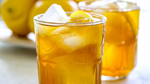 Brown sugar lemonade over ice in two glasses with lemon slices and lemons on the background.