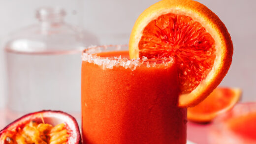 Slice of blood orange on the rim of a glass of our frozen passion fruit mezcalita with fresh passion fruit next to it