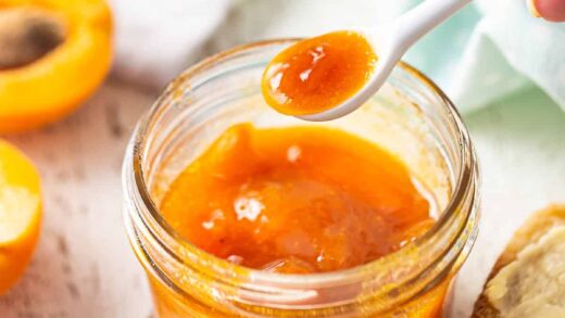 Spooning apricot jam from a glass jar.