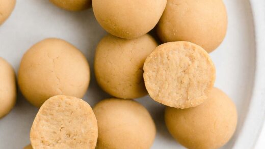 overhead view of no bake peanut butter protein balls on a light gray plate, with one broken in half to reveal the soft texture inside – easy and healthy energy bite recipe – low calorie, low carb, sugar free, vegan, gluten free, dairy free, and clean eating – made with soy protein powder and two types of peanut butter – no sugar, no oats, no dates, no honey