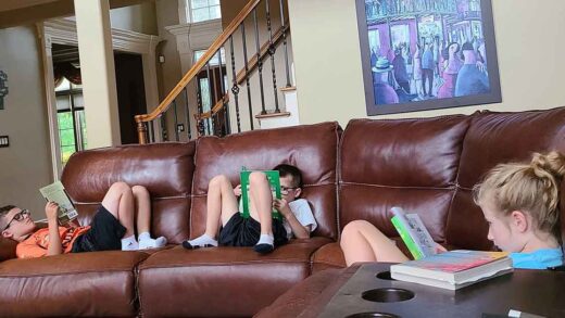 Three kids sitting spread out on a couch, all reading books.