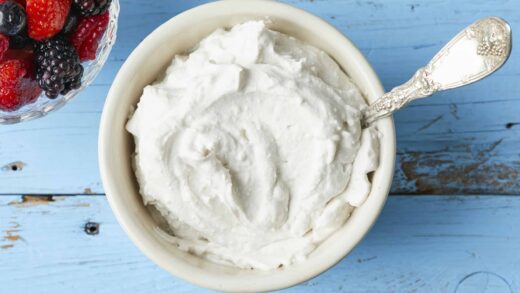 A bowl of thick, creamy coconut whipped cream with a bowl of mixed berries on the side.