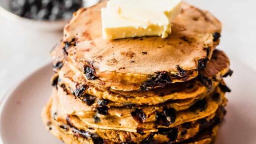 A stack of pumpkin chocolate chip pancakes topped with butter served on a plate.