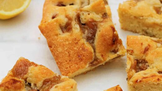 Squares of rhubarb cake on white background, lemon half in background.