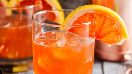 The Campanella - a Paloma Cocktail Variation - old fashioned glass of orange cocktail, another in the background, garnished with half a grapefruit wheel - square cropped image