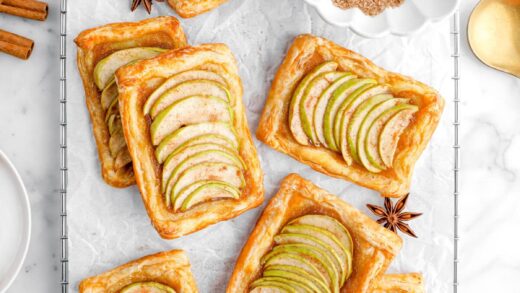 seven mini apple tarts with bowl of cinnamon sugar and spices around.