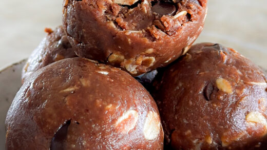 A chocolate oatmeal ball with a bite taken out of it, sitting on top of two other chocolate oat bites in a small white ceramic bowl.