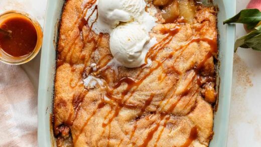 apple cobbler in a blue baking dish with caramel and cinnamon, topped with vanilla ice cream.